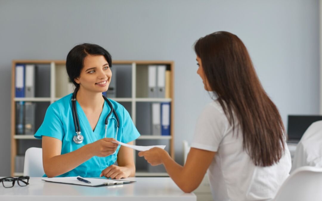 Infermiera in divisa azzurra consegna documento al caregiver di un paziente durante colloquio in ambulatorio